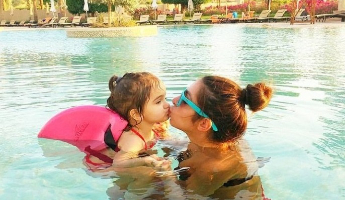 Child wearing SwimFin swimming aid in pool with mother